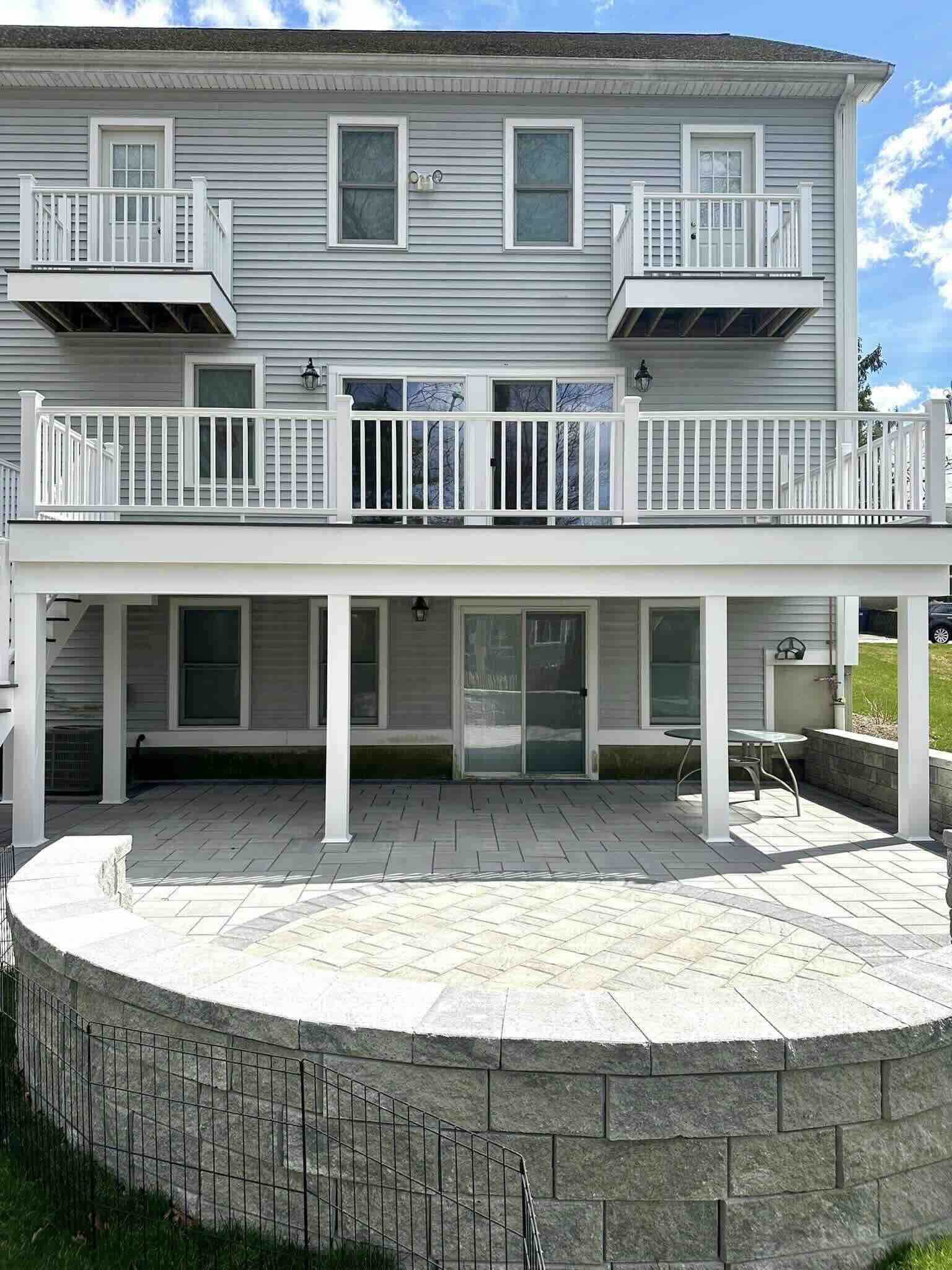 Front view of the elevated deck with white railing and paver patio with bench in worcester ma