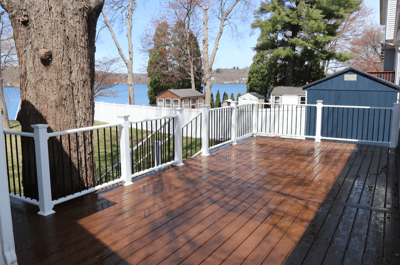 Wet wooden deck with black aluminum railing featuring overlooking nature view in worcester ma